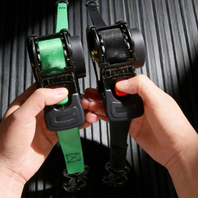 Two ratchet straps, one green and one black, held by hands against a dark background.