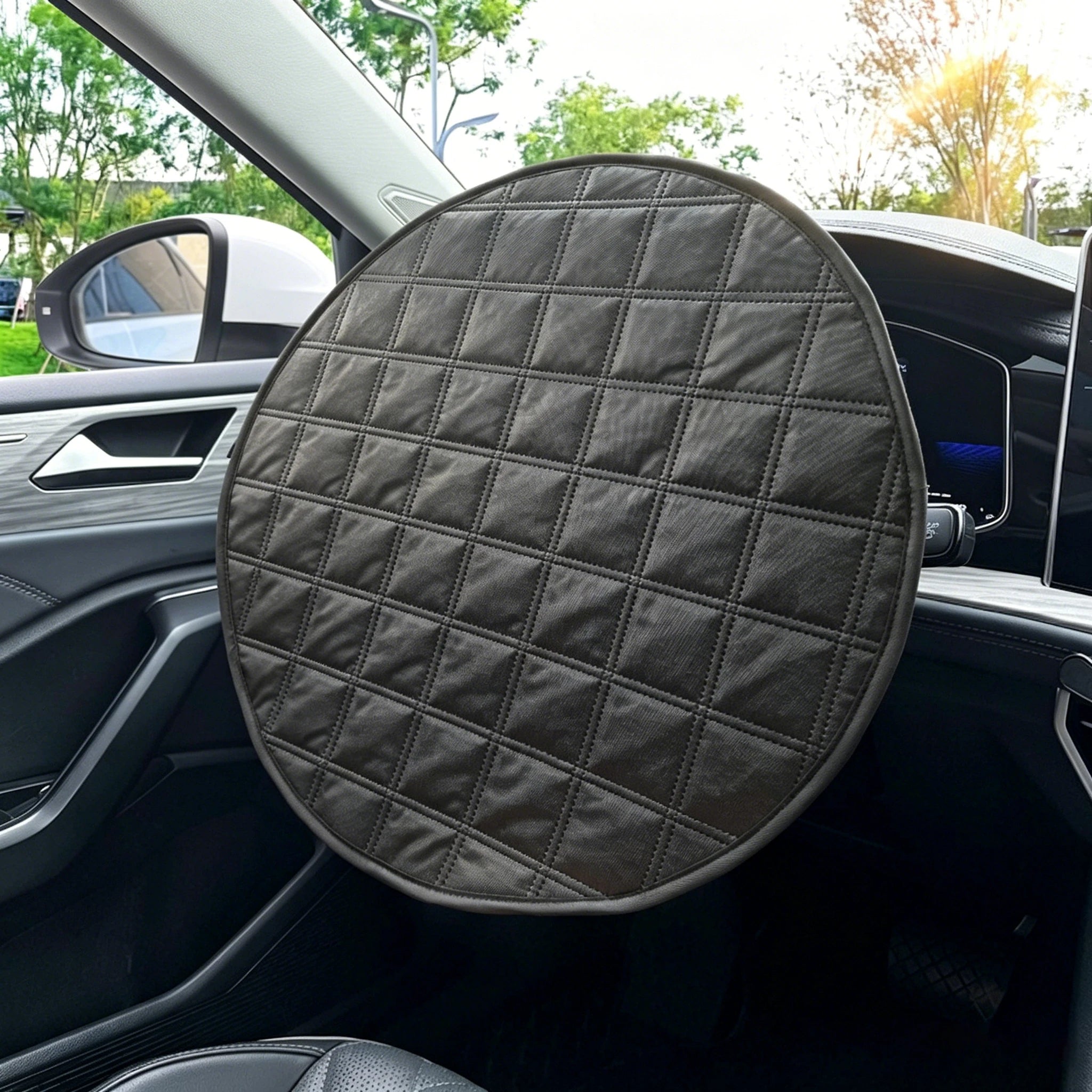 A round black quilted steering wheel cover with a diamond pattern, shown installed on a car's steering wheel inside a vehicle.