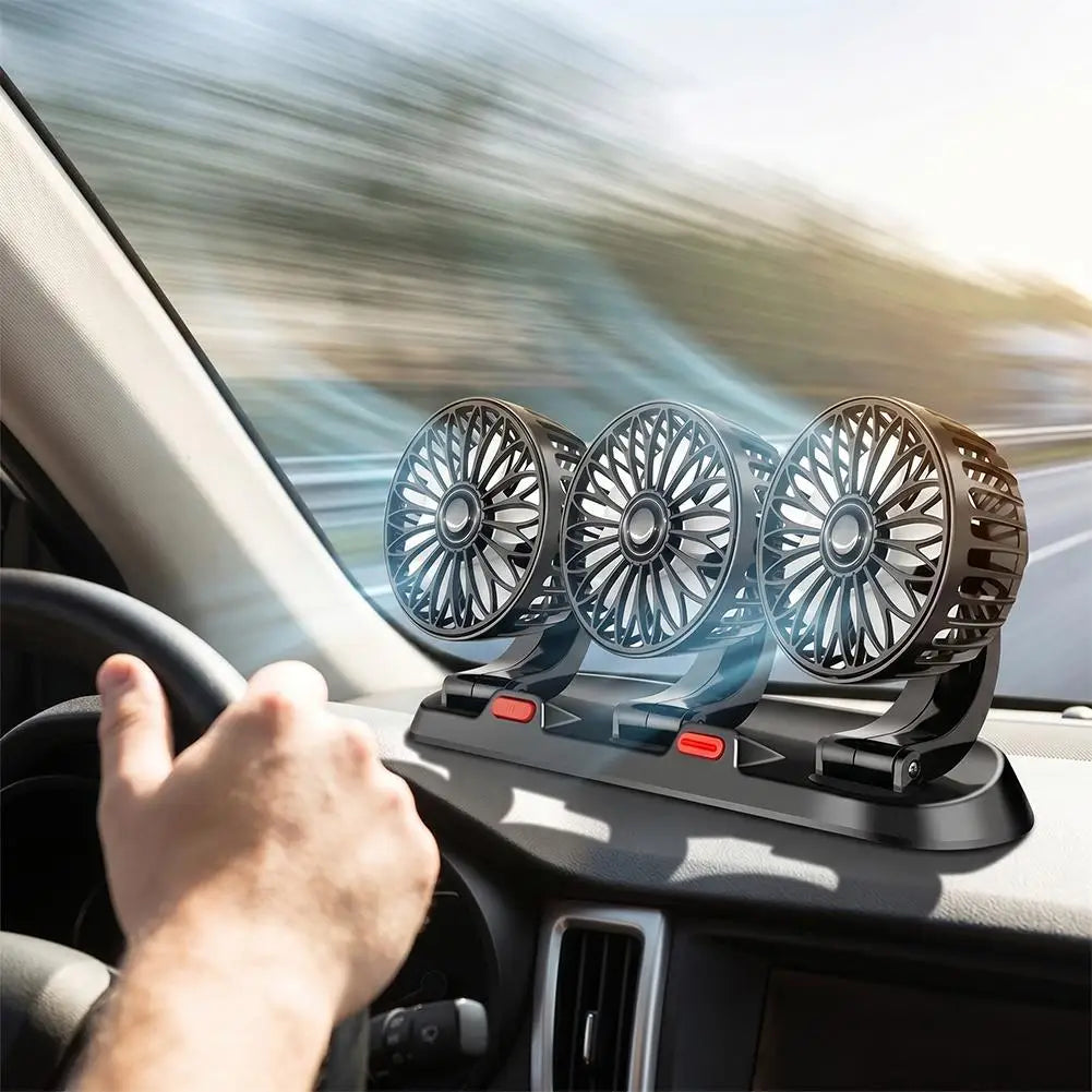 Three small car fans mounted on a dashboard vent console inside a moving vehicle, with a driver's hand visible on the steering wheel and blurred road scenery outside.