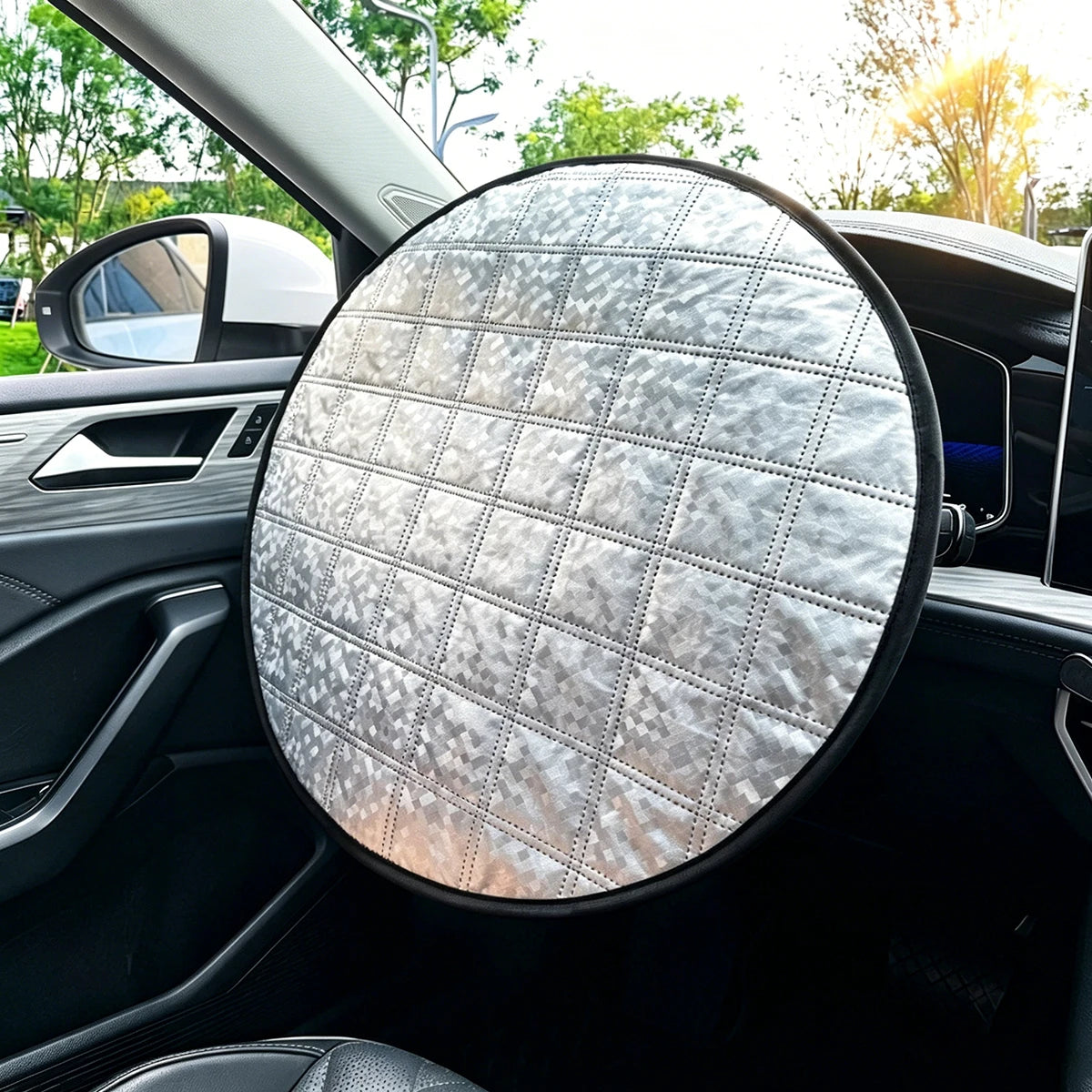 A circular silver quilted car sun shade with a black border, shown attached to the dashboard inside a vehicle.