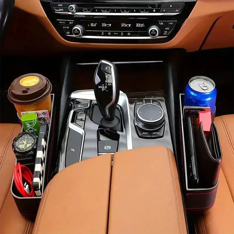 Car interior with gear shift and cup holders containing items like a coffee cup, watch, and snack.
