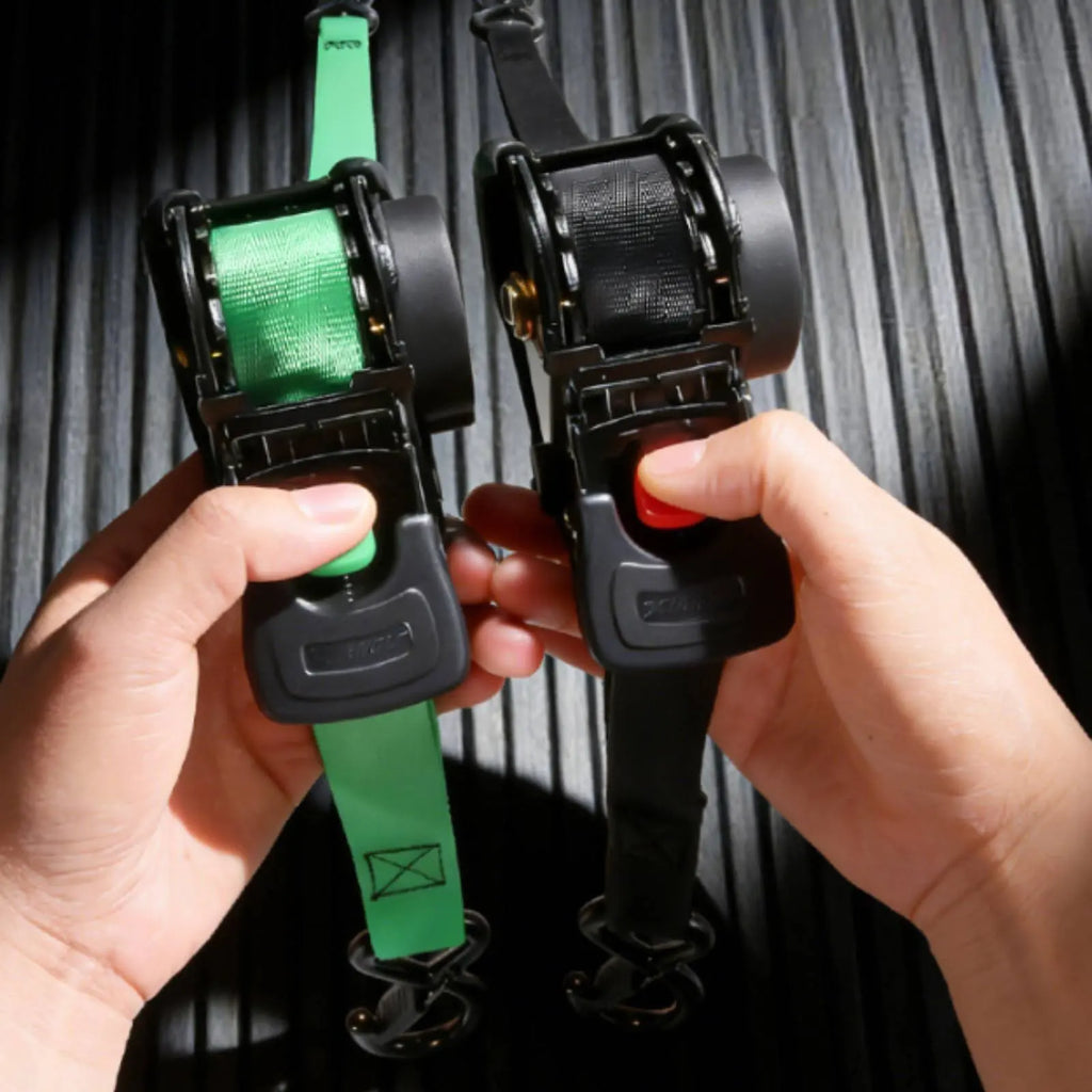 Two ratchet straps, one green and one black, held by hands against a dark background.