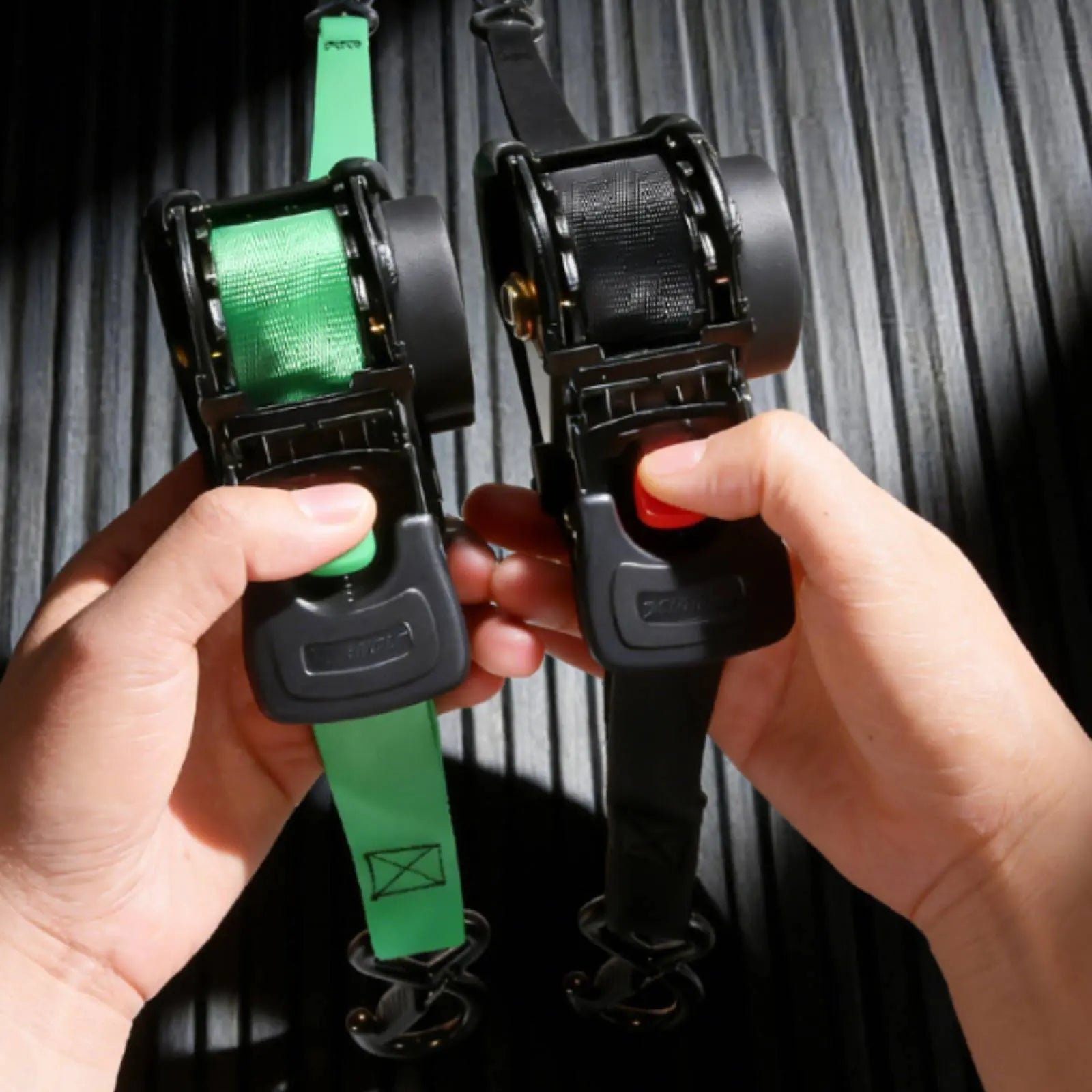 Two ratchet straps, one green and one black, held by hands against a dark background.