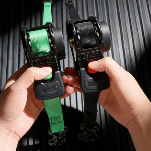 Two ratchet straps, one green and one black, held by hands against a dark background.